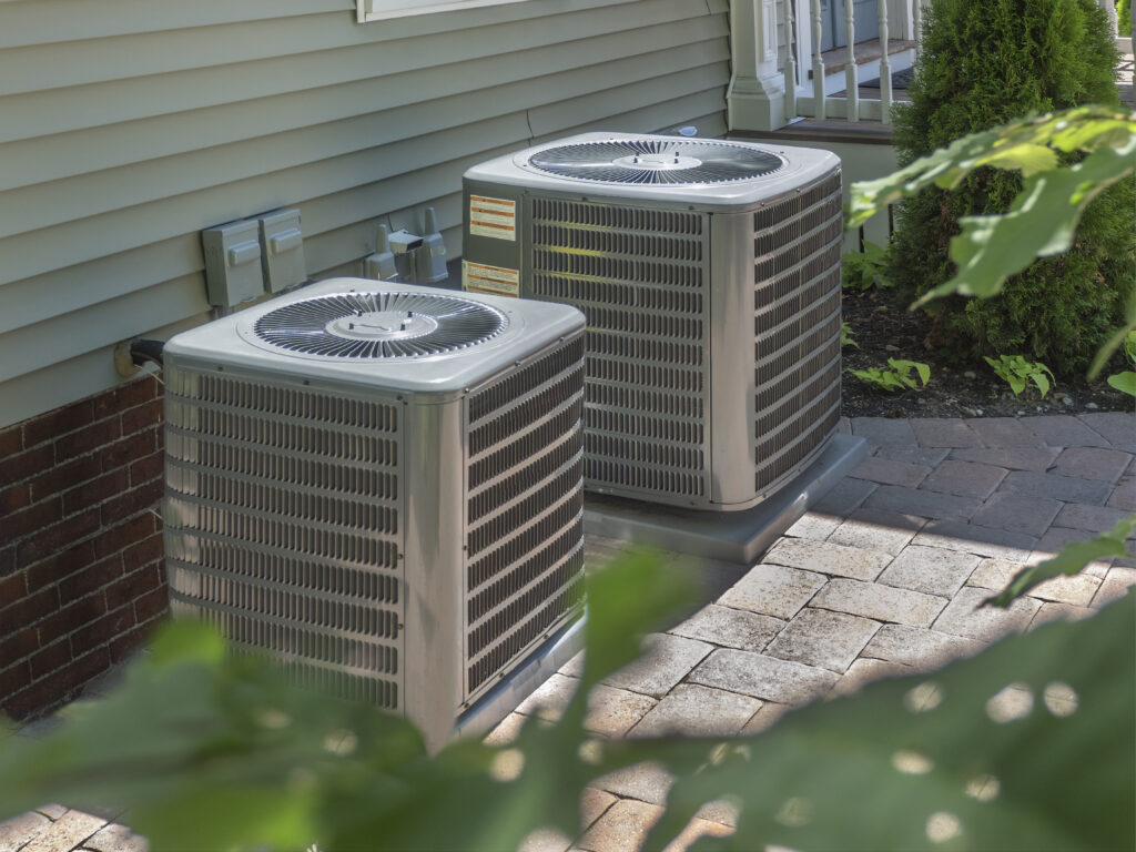 Two HVAC condenser units against a house with exterior siding